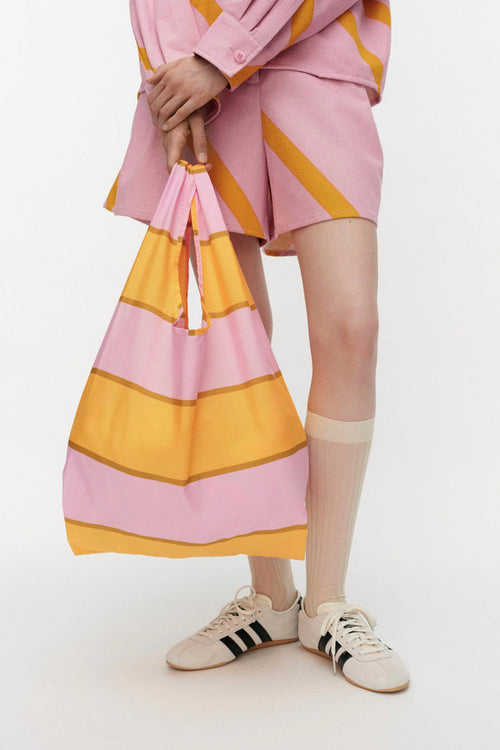 Person wearing a pink outfit with yellow stripes, holding a matching bag on a white background